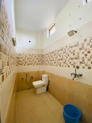 A bathroom with a toilet, shower, and blue bucket. - Hotel KK Hld  (Haldwani)
