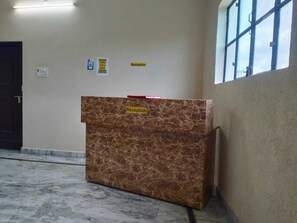 A reception desk with a marble top, a door to the left, and a window to the right. - Hotel KK Hld  (Haldwani)