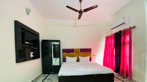 Une chambre d’hôtel équipée d’un lit, d’un ventilateur de plafond, d’un climatiseur, d’une télévision et d’une armoire.