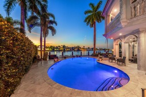 A swimming pool with a curved edge, surrounded by palm trees and a hedge. - The Palazzo | Waterfront | Walk to Beach | Luxury Villa (Fort Lauderdale)