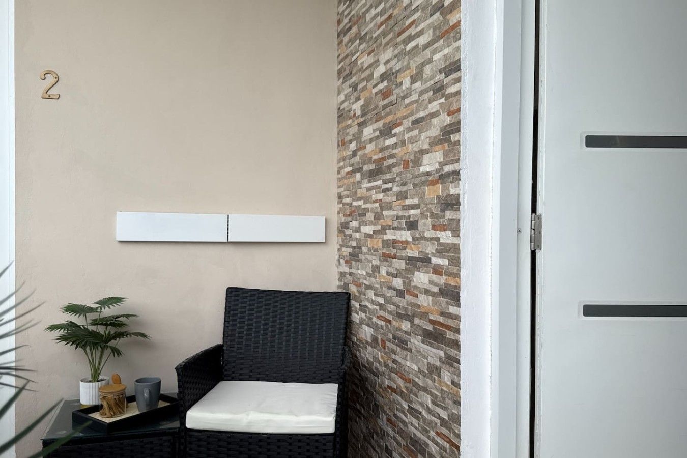 A small room with a wicker chair, a potted plant, and a wall with a stone pattern.