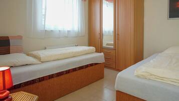A bedroom with two beds, a wardrobe, a window with curtains, and a bedside table with a lamp.
