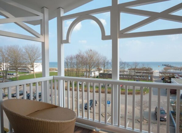 A balcony with a wicker chair, white railings, and a view of the sea and buildings. - Holiday Apartment With 1 Bedroom (Grossenbrode)