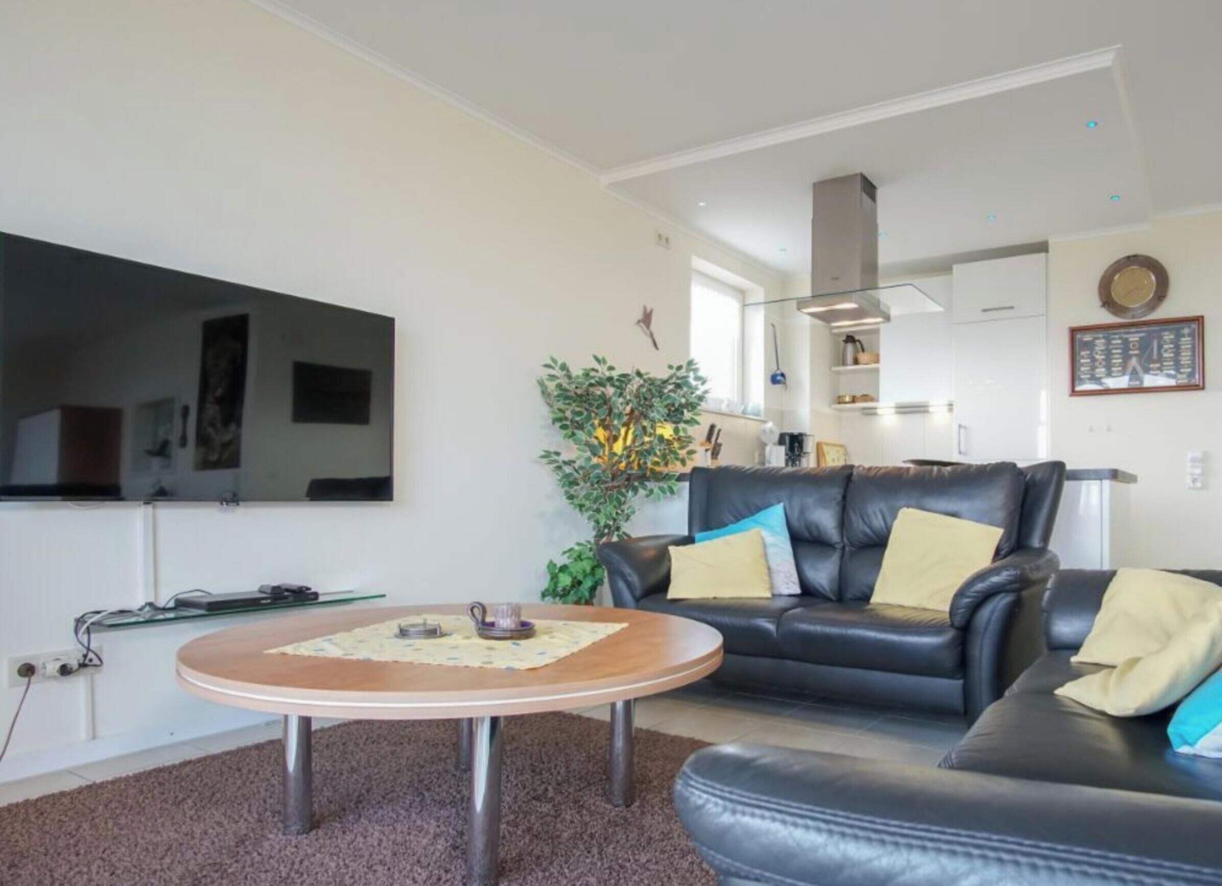A living room with a black leather sofa, a round coffee table, and a flat-screen TV mounted on the wall.