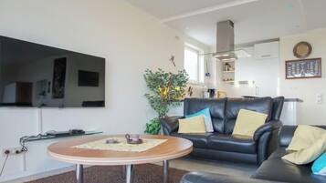 A living room with a black leather sofa, a round coffee table, and a flat-screen TV mounted on the wall.