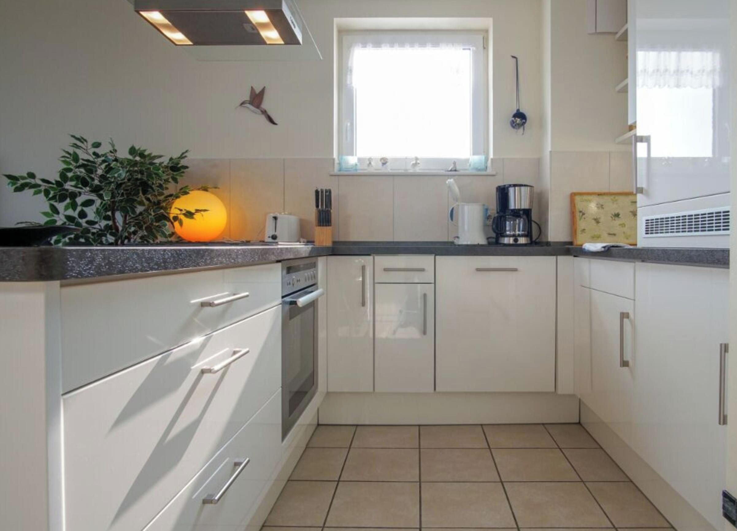 A modern kitchen with white cabinets, a built-in oven, and a window above the sink.
