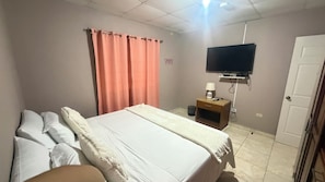 Una habitación de hotel con una cama, una mesita de noche, un televisor y una puerta.