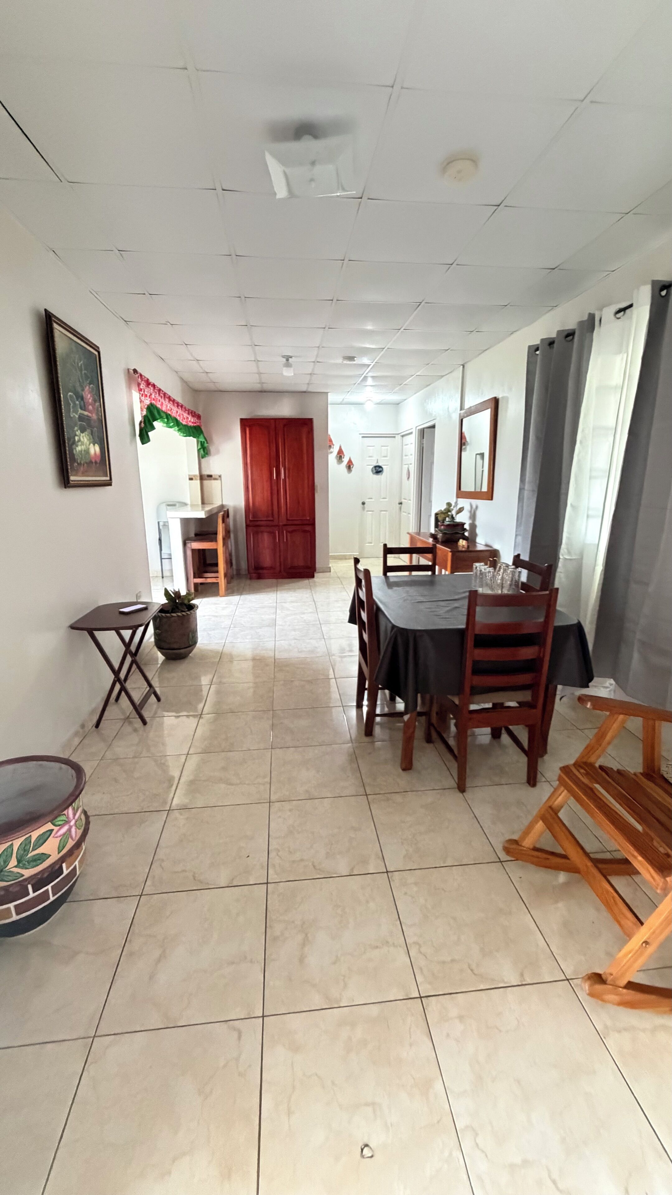 Un comedor con suelo de baldosas, sillas de madera, una mesa con mantel negro y una planta en maceta.