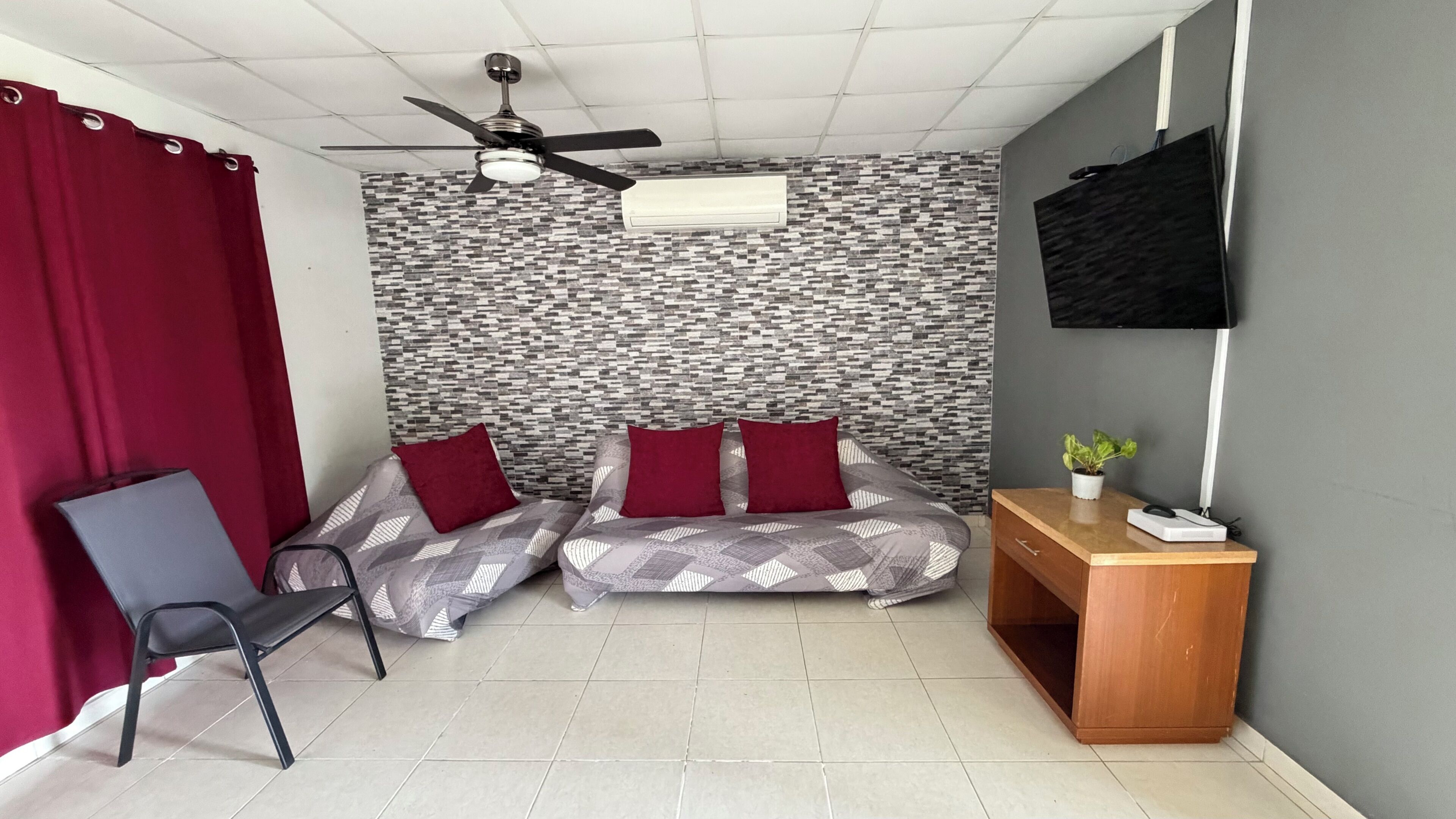 Una habitación con cama, escritorio, silla, ventilador de techo y televisor.