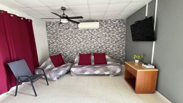 Une chambre avec un lit, un bureau, une chaise, un ventilateur de plafond et un téléviseur.