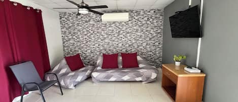 A room with a bed, a desk, a chair, a ceiling fan, and a TV.
