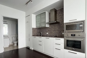 A modern kitchen with white cabinets, a brick backsplash, and stainless steel appliances including a microwave and oven. - Basic Queen Studio Suite at The Velaire Toronto (Toronto)