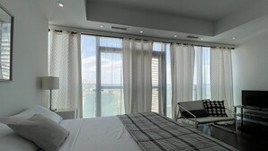 Ein modernes Hotelzimmer mit einem großen Bett, einem Schreibtisch, einem Sessel und einem Fernseher.