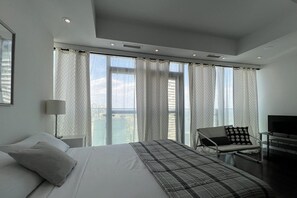 A modern hotel room with a large bed, a desk, a chair, and a TV. - Basic Queen Studio Suite at The Velaire Toronto (Toronto)