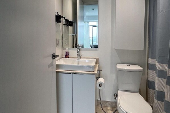 A compact bathroom with a white sink, mirror, and toilet. - Basic Queen Studio Suite at The Velaire Toronto (Toronto)