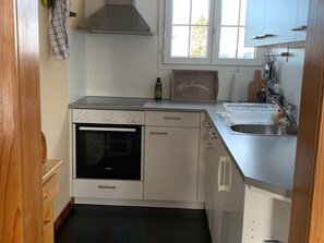A compact kitchen with a built-in oven, a stainless steel sink, and a window above the countertop.