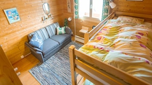 Quarto de cabana de madeira com uma cama, um sofá, uma mesinha, um espelho e uma janela com cortinas.