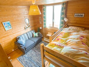 Ein Schlafzimmer einer Holzhütte mit einem Bett, einer Couch, einem kleinen Tisch, einem Spiegel und einem Fenster mit Vorhängen.