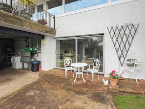 Un immobile residenziale con patio attrezzato da tavolo e sedie, una porta scorrevole che dà su una cucina e un balcone con ringhiera.