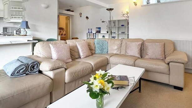 A modern living room with a beige sectional sofa, a white coffee table, and a vase of flowers. - Apartment Sleeps 2 with Parking, Pets Welcome (Penrith)