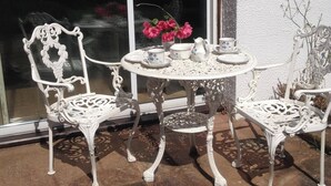 A white outdoor seating area with a table and chairs, a vase with flowers, and a window with a view of the landscape. - Apartment Sleeps 2 with Parking, Pets Welcome (Penrith)