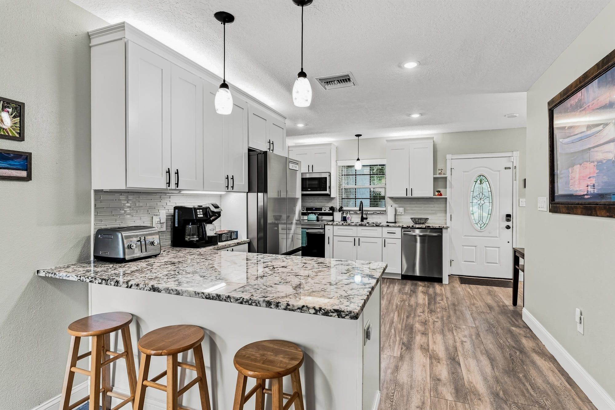 A modern kitchen with white cabinets, granite countertops, and stainless steel appliances. There are two wooden stools at the island.