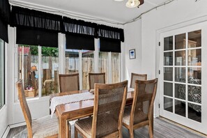 A dining area with a wooden table and four chairs, a black valance over the windows, and a view of a garden through the glass doors. - 🌸Pinellas Paradise - 4BR Pinellas Park home with pool| Sleeps 10 🌸 (Pinellas Park)