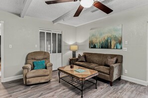 A living room with a ceiling fan, a sofa, a chair, a coffee table, and a painting on the wall. - 🌸Pinellas Paradise - 4BR Pinellas Park home with pool| Sleeps 10 🌸 (Pinellas Park)