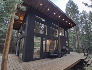 A modern two-story cabin with large windows, a deck, and a staircase leading to the upper level. - Rewild Cabin-Modern Cabin Sanctuary with Valley Views, Firepit & Wraparound Deck (Santa)