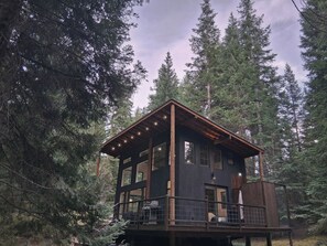 A cabin with a balcony, surrounded by tall trees.