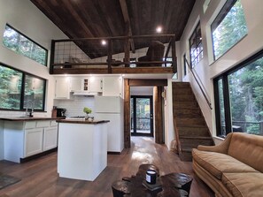 A spacious kitchen with a central island, wooden beams, and large windows offering views of the outdoors. - Rewild Cabin-Modern Cabin Sanctuary with Valley Views, Firepit & Wraparound Deck (Santa)