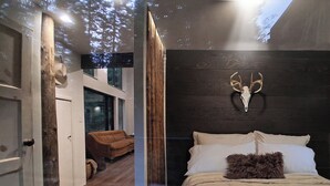 Un dormitorio con cama, cabecera de madera, cráneo de animal montado en la pared y ventana con vista a árboles.