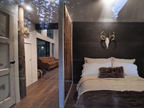 A bedroom with a bed, a wooden headboard, a mounted animal skull, and a window with a view of trees. - Rewild Cabin-Modern Cabin Sanctuary with Valley Views, Firepit & Wraparound Deck (Santa)