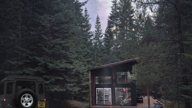 Una cabaña con terraza y fogón, rodeada de un bosque denso.