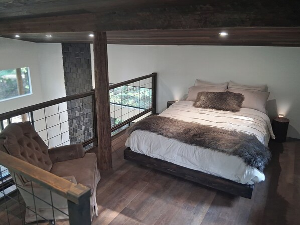 A bedroom with a bed, a chair, a nightstand, and a view through a window.