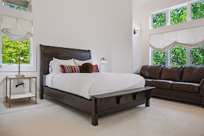 A bedroom with a bed, a bedside table, a lamp, a sofa, and large windows with curtains. - Kai|Ridge At The Running Y (Klamath Falls)