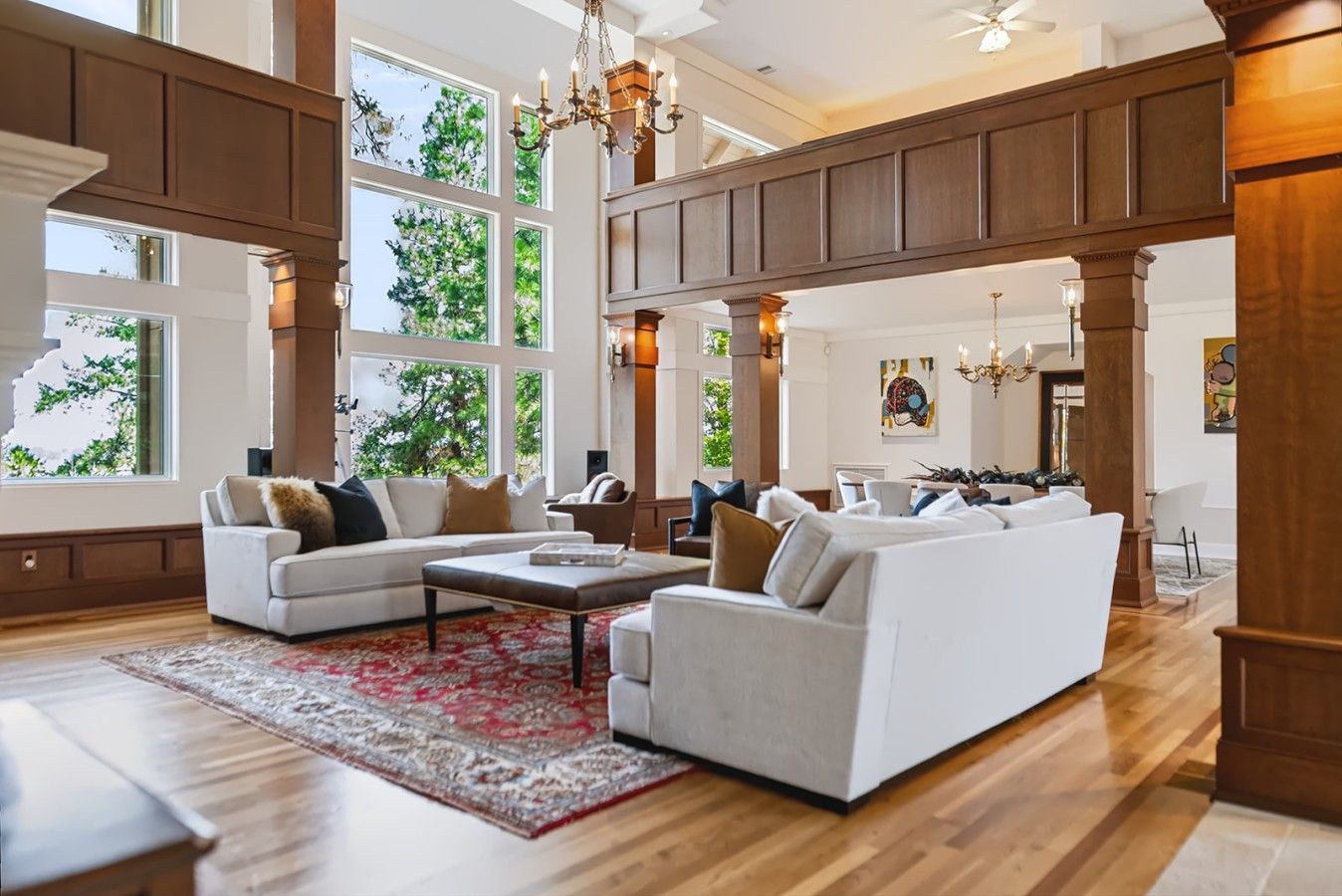 A spacious living room with a high ceiling, large windows, and a grand wooden staircase.