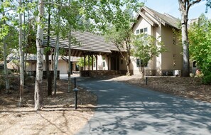 A building with a covered walkway, surrounded by trees and a paved path. - Kai|Ridge At The Running Y (Klamath Falls)