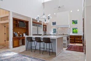 A modern kitchen with a central island, bar stools, a chandelier, and a ceiling fan. - Kai|Ridge At The Running Y (Klamath Falls)