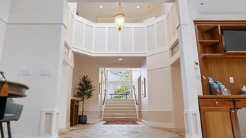 A spacious interior with a staircase leading to an upper level, a chandelier, and a wooden cabinet with magazines.