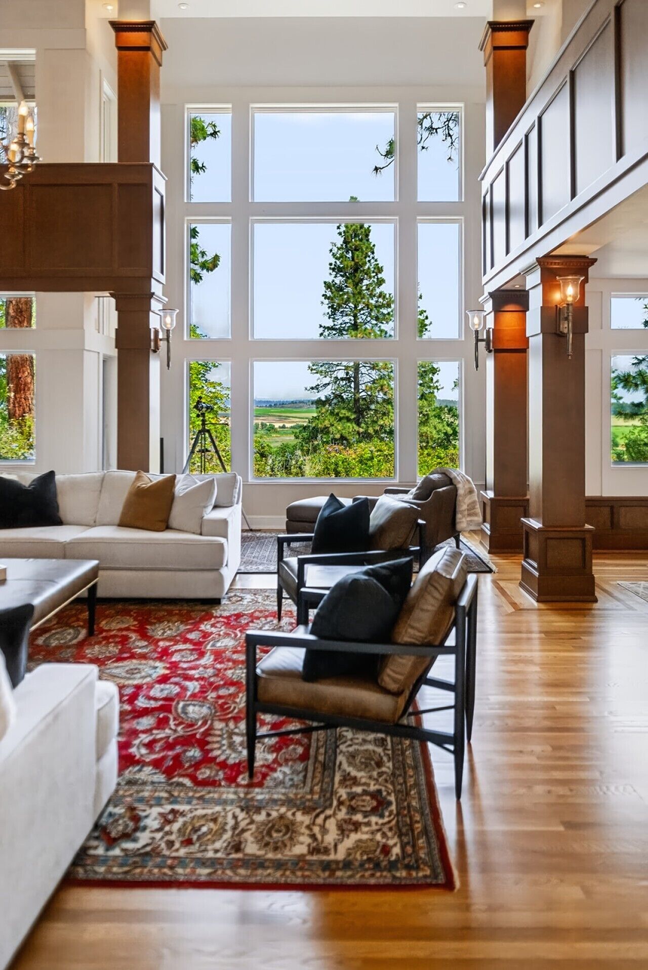 A spacious living room with a large window, a red patterned rug, and a wooden floor.