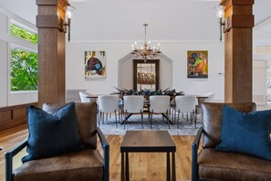 A dining area with a wooden table, white chairs, and a chandelier. There are two large columns and artwork on the walls. - Kai|Ridge At The Running Y (Klamath Falls)