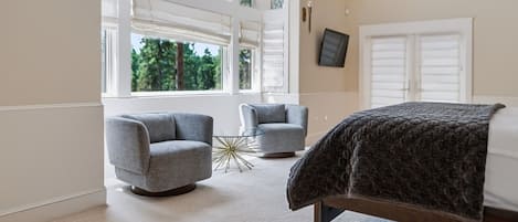 Un dormitorio con cama, dos sillones, una mesita de cristal y ventanas amplias.