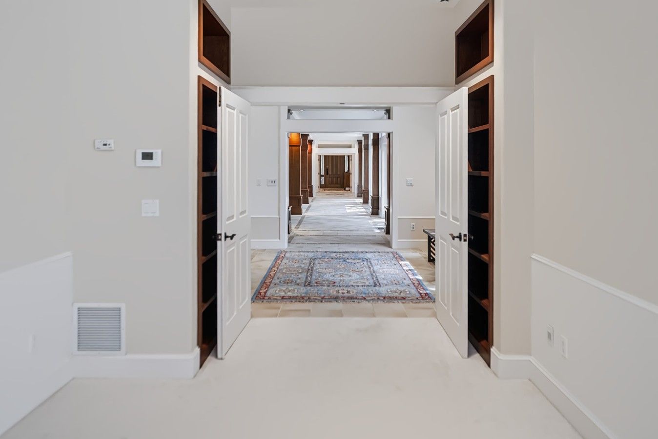 A hallway with white walls, wooden doors, and a patterned carpet.