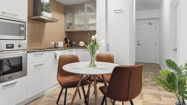 A modern kitchen with white cabinetry, a built-in oven, and a dining area with a round table and brown chairs.