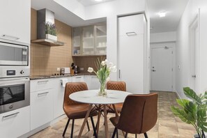 A modern kitchen with white cabinetry, a built-in oven, and a dining area with a round table and brown chairs. - Executive 1BR Hotel Suite with Sofa Bed | Toronto (Toronto)