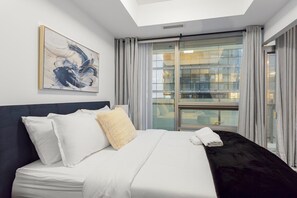 A hotel room with a bed, a painting on the wall, and a view through a large window. - Executive 1BR Hotel Suite with Sofa Bed | Toronto (Toronto)