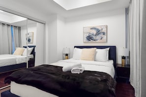 A hotel room with a bed, bedside lamps, a mirror, and a painting on the wall. - Executive 1BR Hotel Suite with Sofa Bed | Toronto (Toronto)
