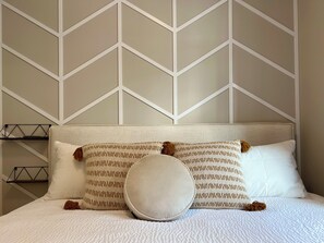 A bed with a textured white headboard, two patterned pillows, and a round pillow. - Separate-Address Combo • Hot Tub • Parking • Air Conditioner, Sleeps up to 17 (Harvie Heights)