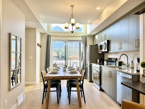 A modern kitchen with a dining area, large windows, and a view of mountains. - Separate-Address Combo • Hot Tub • Parking • Air Conditioner, Sleeps up to 17 (Harvie Heights)